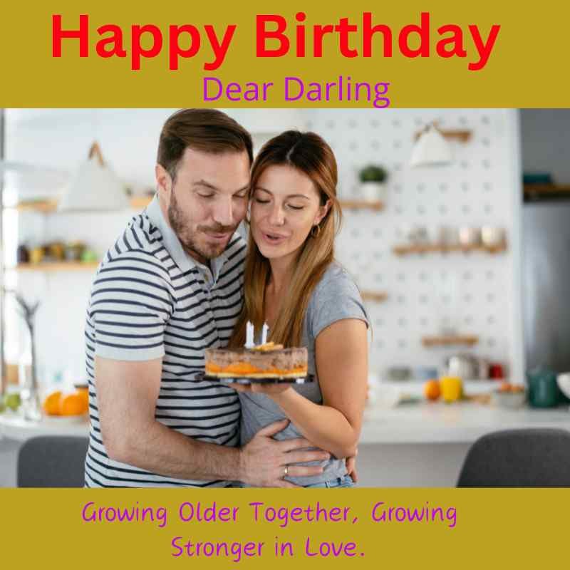 Couple embracing in kitchen while holding birthday cake with candles.