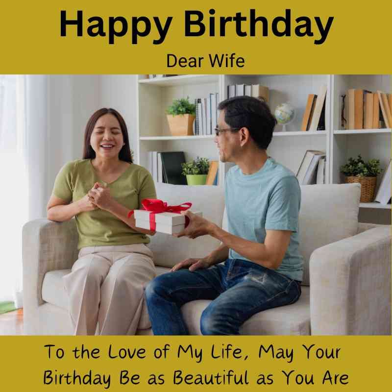 Husband giving a birthday gift to his smiling wife on a couch.