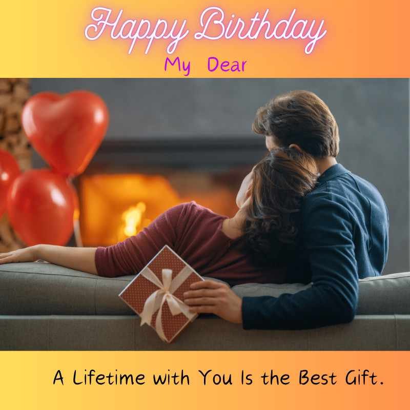 Couple cuddling on couch with gift and balloons by fireplace on birthday.