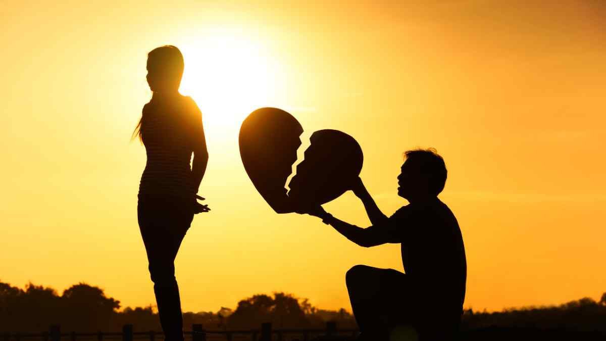 Silhouette of a man holding a broken heart toward a woman at sunset, symbolizing heartbreak